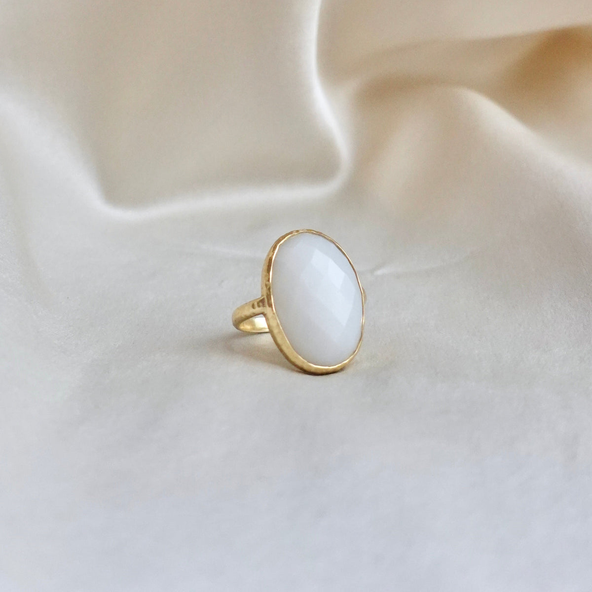An 18K gold ring with a large oval white faceted chalcedony, set in a thin bezel with a hammered-textured band.