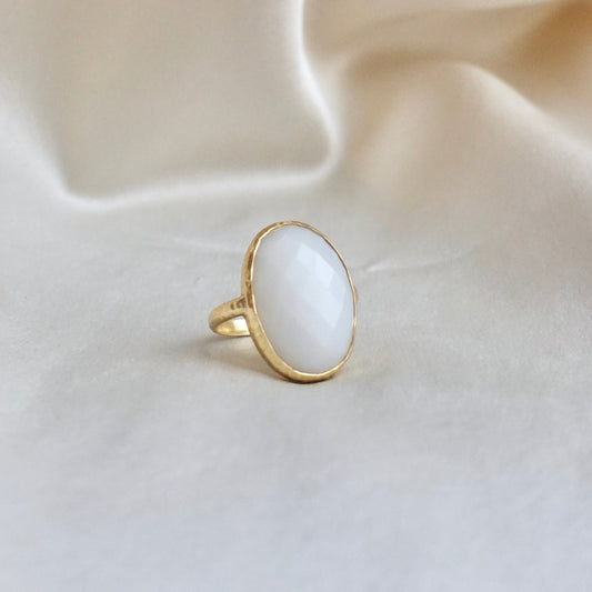 An 18K gold ring with a large oval white faceted chalcedony, set in a thin bezel with a hammered-textured band.