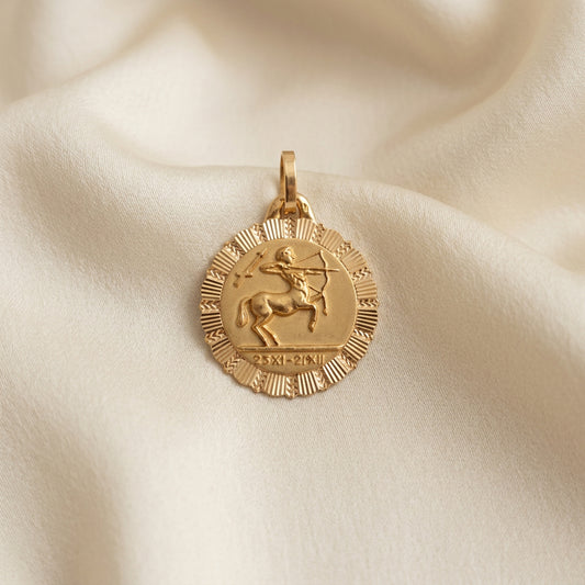 A round gold Sagittarius  pendant with a textured outer rim, with a saytr in the center and roman dates for sagittarius' star sin at the bottom of the pendant